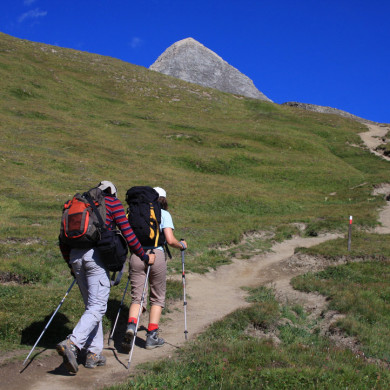 Deux randonneurs équipés de sacs et bâtons marchant sur un sentier de montagne
