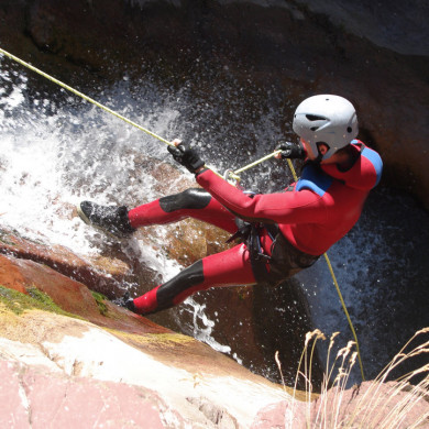 Sportif en combinaison et casque pratiquant le canyoning en descente de cascade
