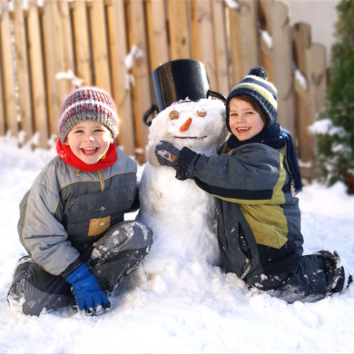 Deux enfants construisent un bonhomme de neige au village vacances Azureva Bussang