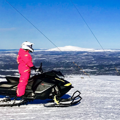 Personne en combinaison rose conduisant une motoneige aux Karellis avec vue sur les montagnes enneigées